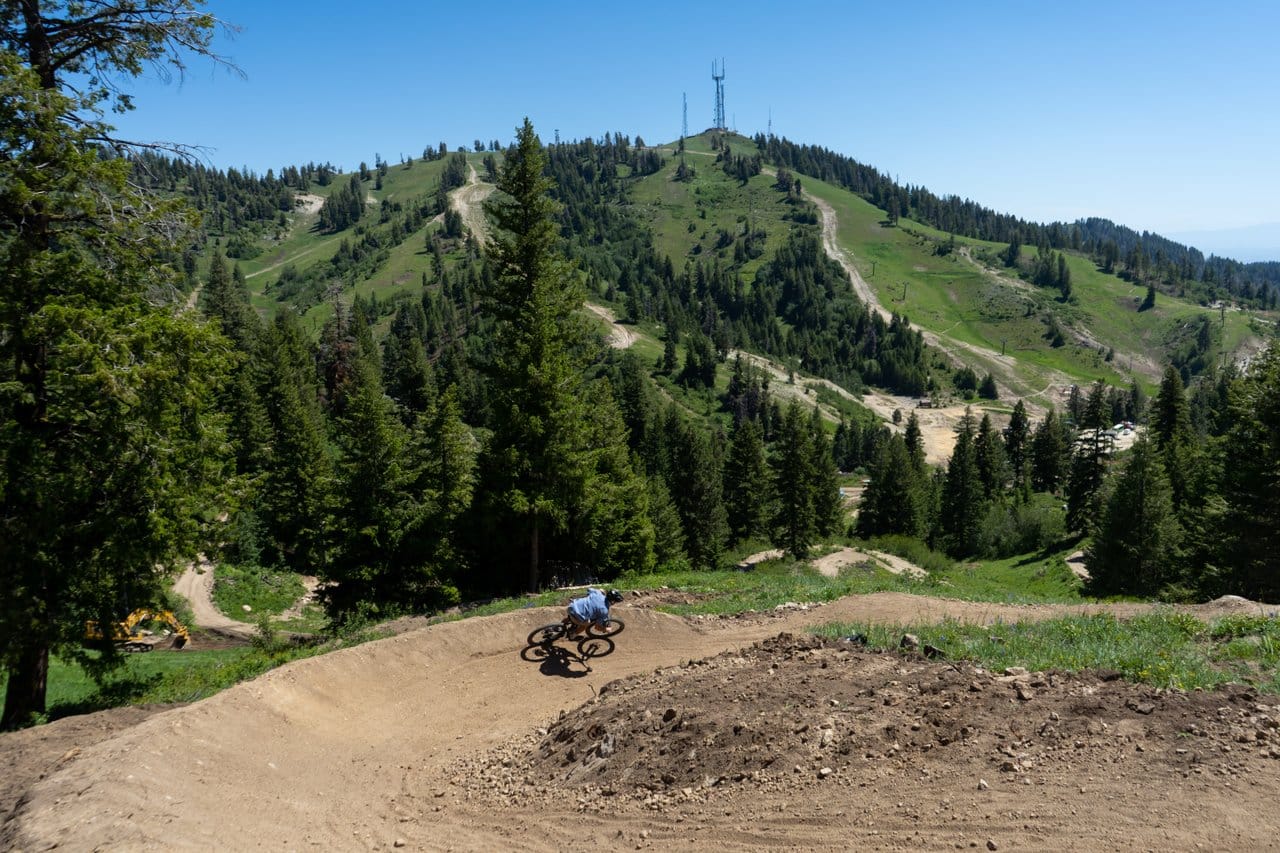 man mountain biking on a corner with green mountains in the background at bogus basin